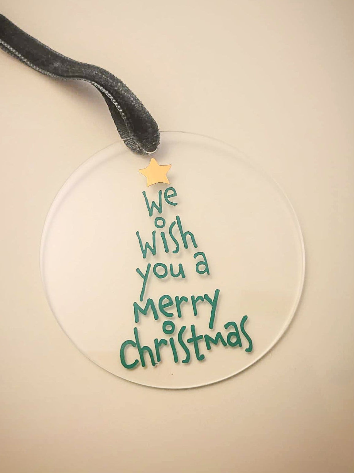 Round Christmas ornament with 'We wish you a Merry Christmas' text on a beige background