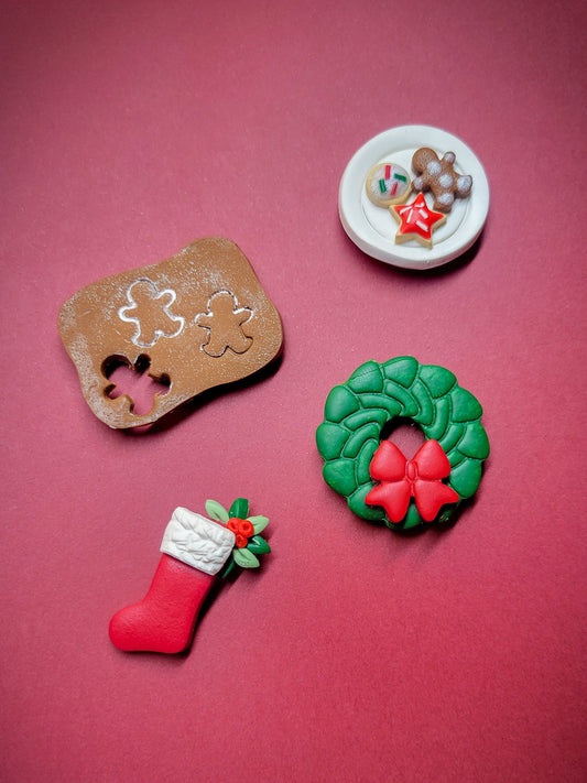 4 mini magnets made of polymer clay: 1 plate of cookies, 1 gingerbread board, 1 green wreath with red bow, and 1 stocking with holly berries. 