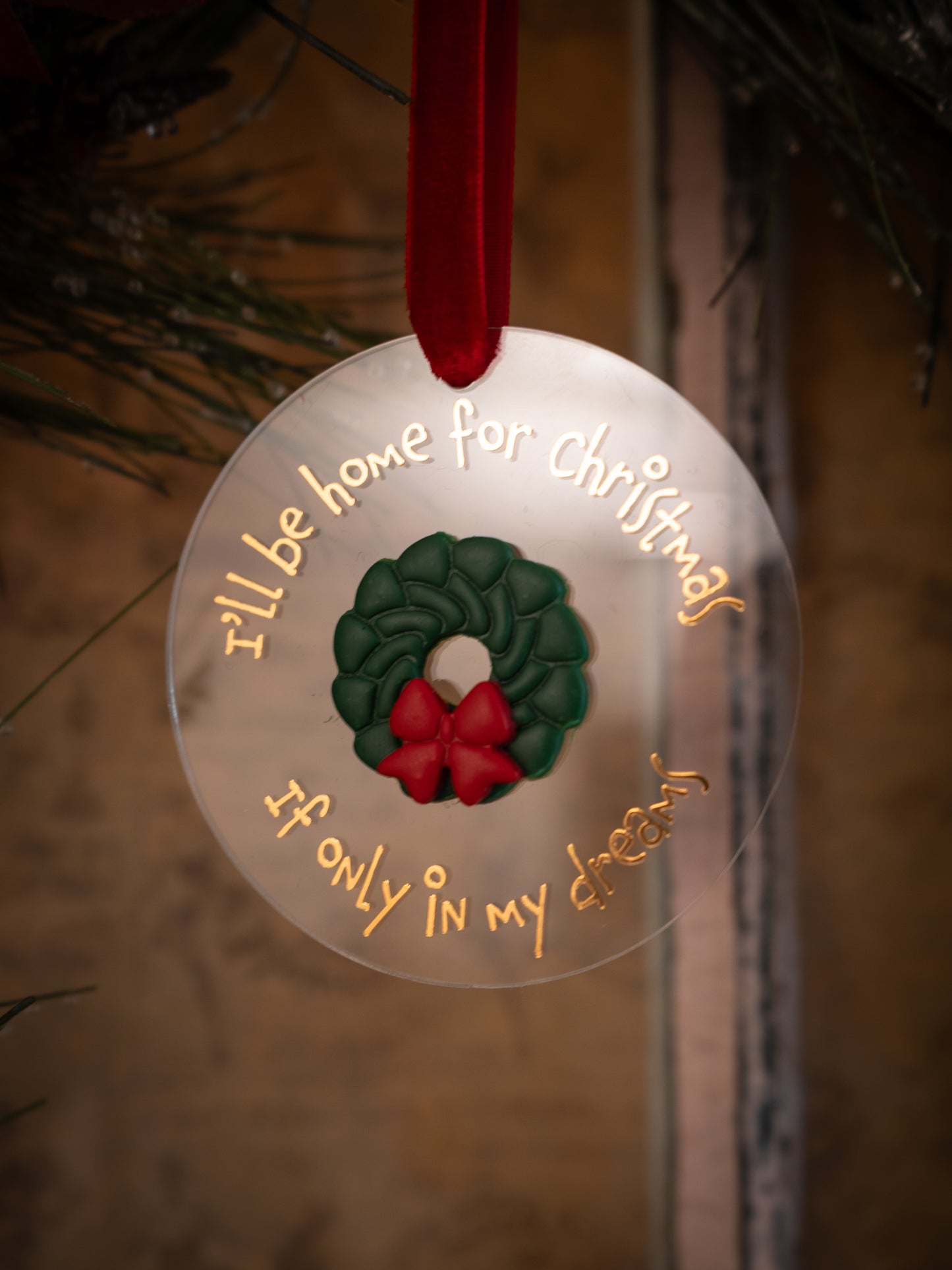 Christmas ornament with wreath and text 'I'll be home for Christmas if only in my dreams' on a blurred background.